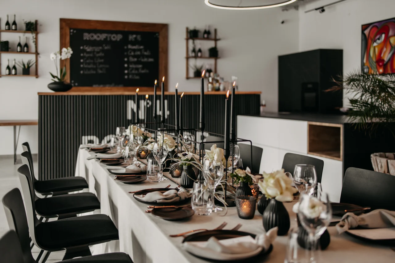 Lange festlich gedeckte Tafel mit Blick in den Eventraum und zur Bar